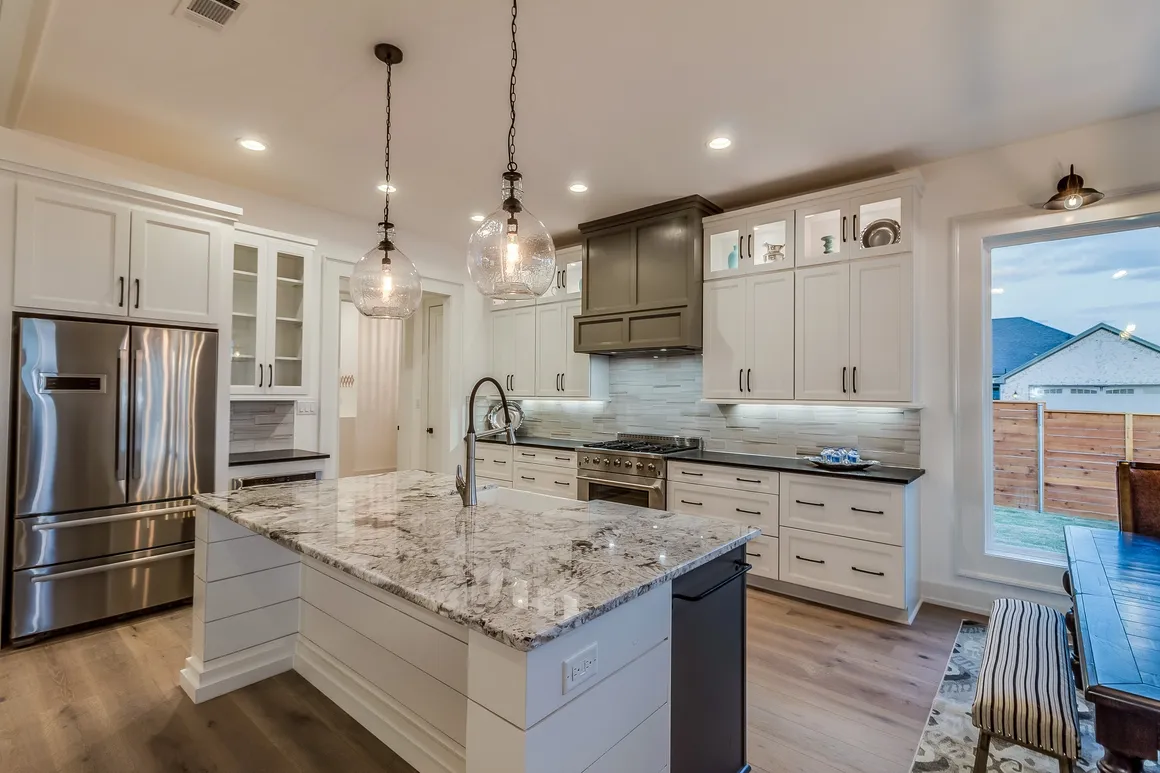 Modern white kitchen with center island, stainless steel appliances, and pendant lights