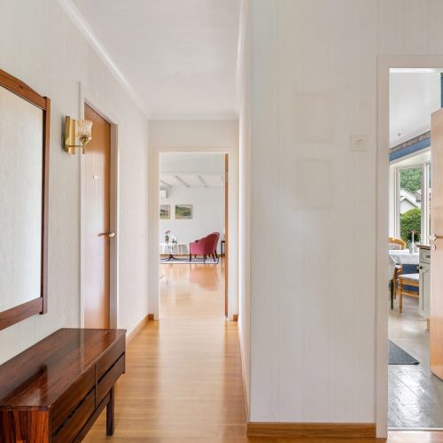 A well-lit modern hallway with open doors leading to a bright living area and garden view.