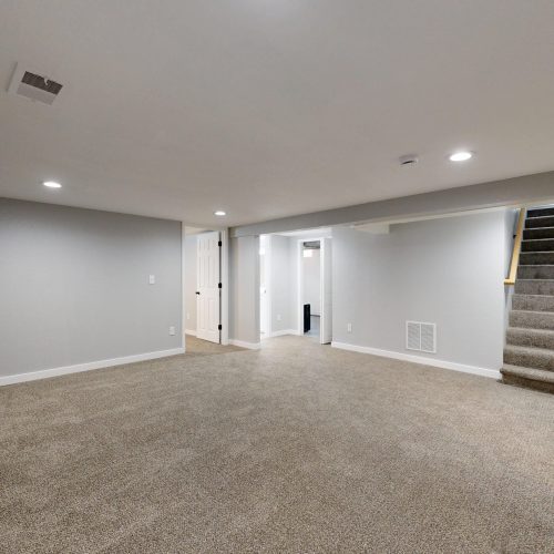 Empty modern basement with beige carpet and white walls, ideal for renovation.
