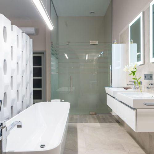 White bathtub with tap near decorative partition placed near sink and mirrors in stylish light bathroom with glass shower cabin